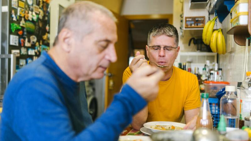 Older male couple eating meal together in home kitchen