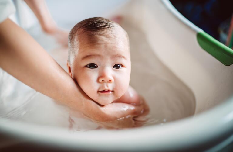 newborn baby held by mother's hands in small bathtub