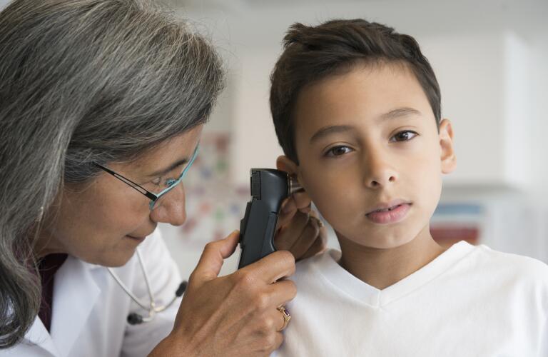 Young Hispanic boy having ear checked by older female doctor