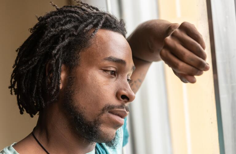 Young African American man looking out window with worry or sadness