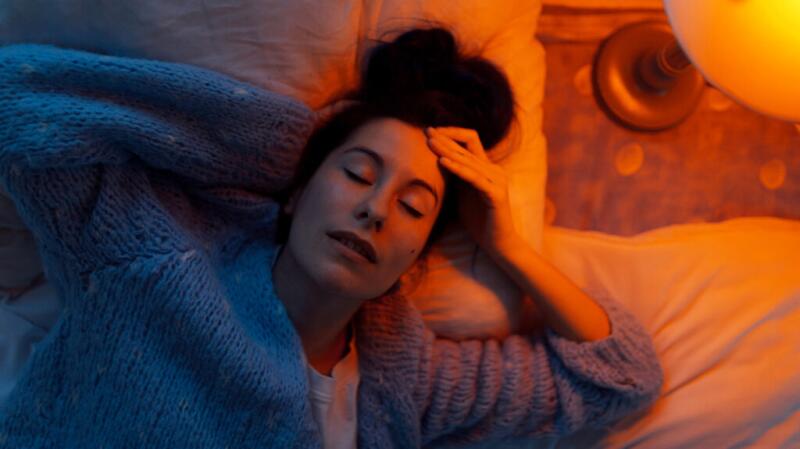 Woman lying in bed with eyes closed and mouth slightly open in orange tinted lighting