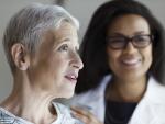 Older Caucasian female patient in hospital gown with smiling African American female doctor