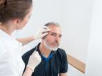 dermatologist examining an age spot or skin lesion on man's forehead