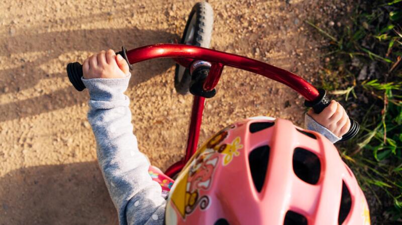 An aerial view of a toddler riding a tricycle while wearing a helmet.