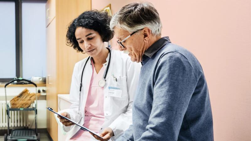 Older male patient talking with female doctor while looking at chart