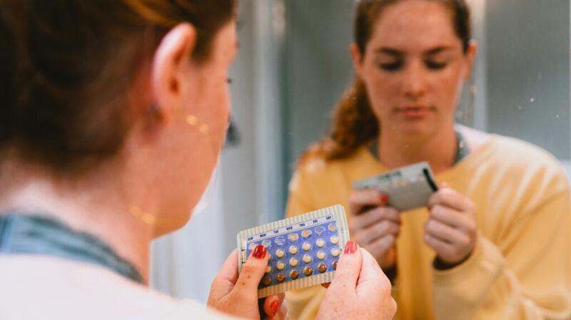 A person holds a sheet of birth control pills and reads the dates.
