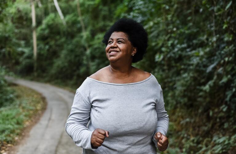 smiling African American woman walking or jogging through forest trail