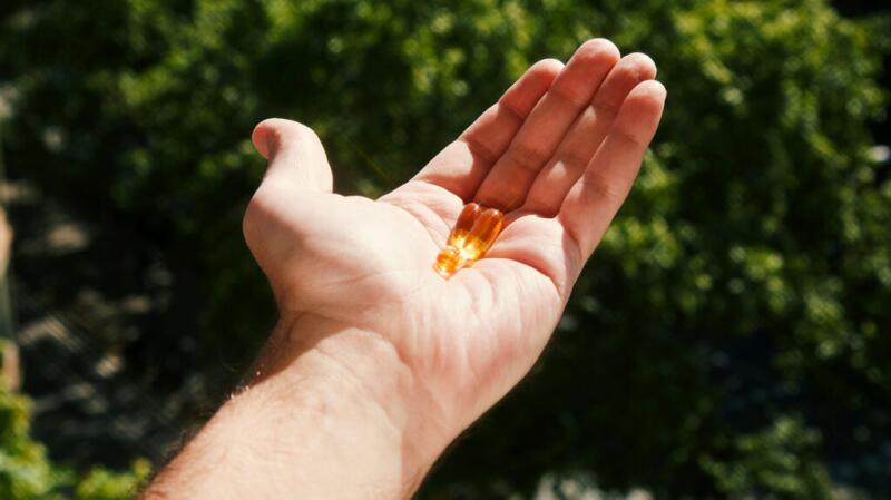 An open hand holds three clear capsules.