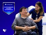 Stock image featuring a young female doctor wearing blue scrubs pushing a male patient in a wheelchair down a hospital corridor. To the left of the stock image, a 2025 Healthgrades Outstanding Patient Experience Award is superimposed against a blue gradient background.