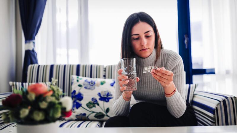 a woman is sat on a sofa taking an antacid