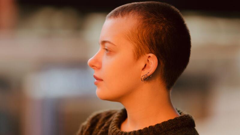 Person sits with their head to the side against a blurred background, showing the side profile of their head and face.