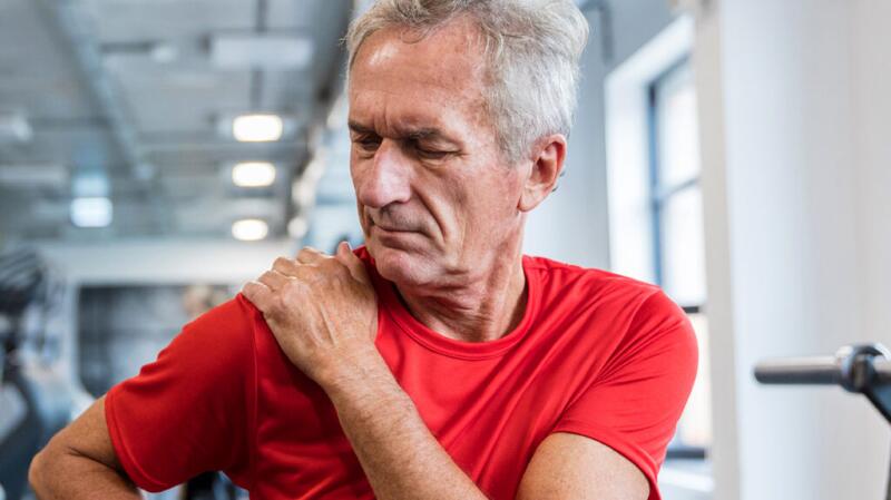 Male in a red t-shirt grabbing his shoulder in gym
