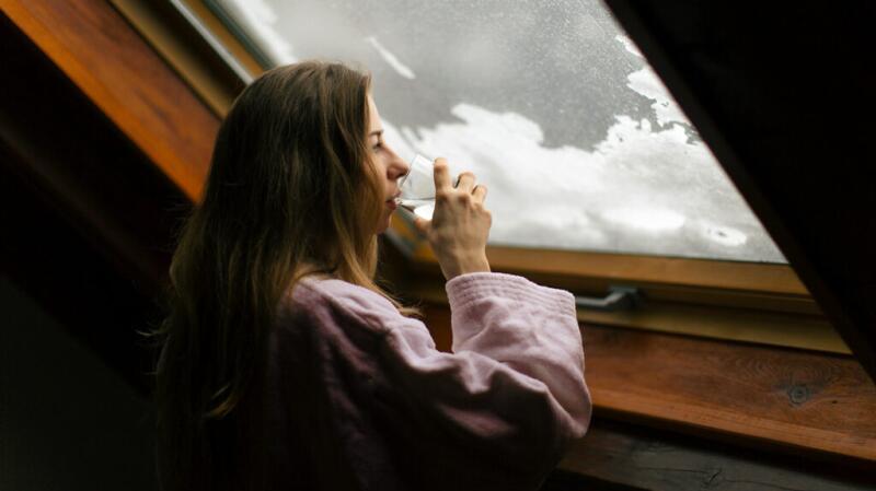 a person is drinking water and looking out of a window