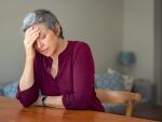 Senior Caucasian woman at table with head on hand from stress, fatigue or migraine headache