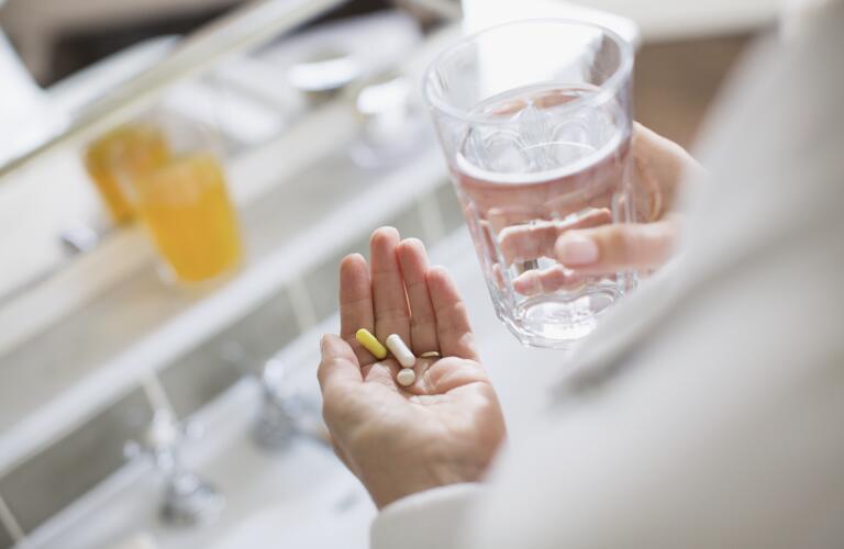 Unseen Caucasian woman's hands holding pills in left hand and glass of water in right hand