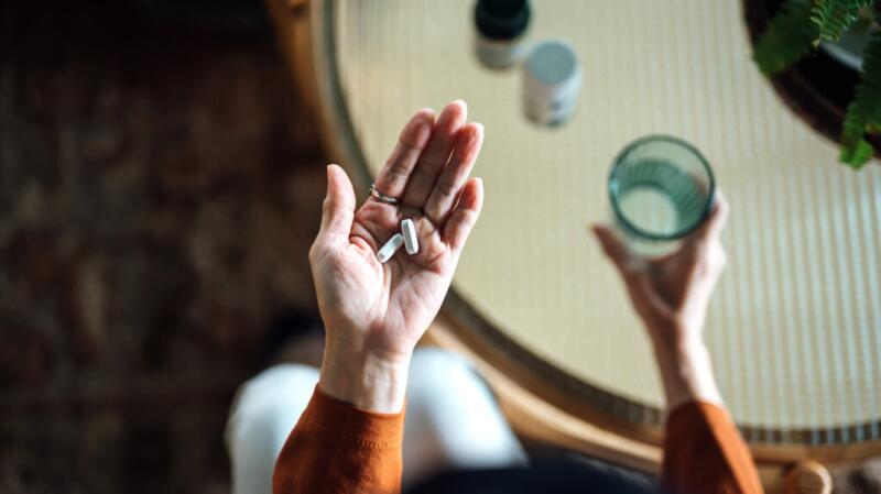a person is taking a supplement pill with a glass of water