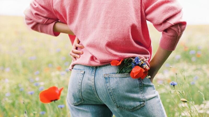 Person stands in field of flowers holding lower back and hip