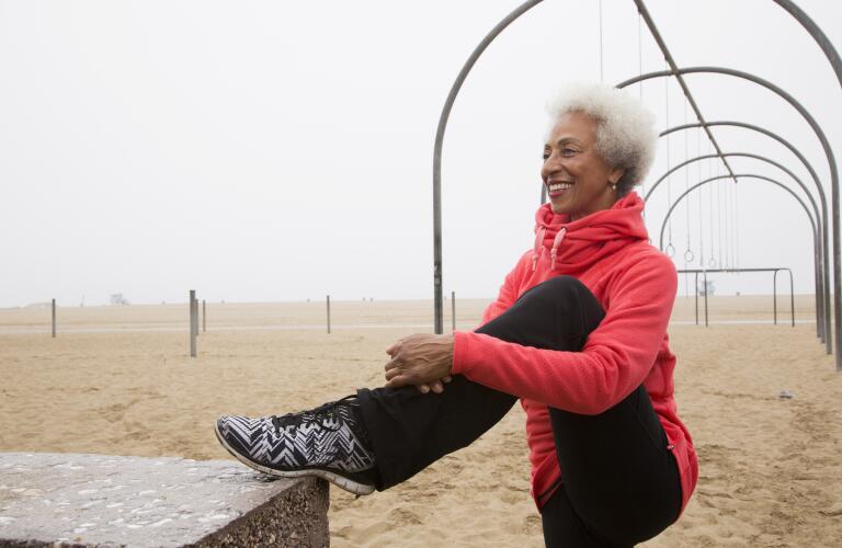 african american senior woman stretching on beach
