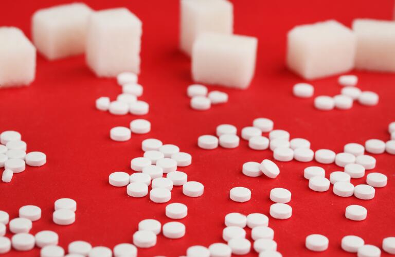 Glucose tablets on red surface with sugar cubes in background
