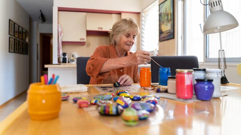 Older woman painting rocks on kitchen table