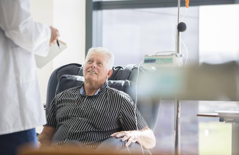 senior Caucasian male receiving chemotherapy in hospital speaking with doctor