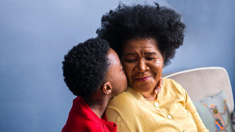 Grandson is kissing their grandmother on the cheek