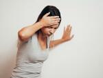 woman suffering from vertigo or dizziness with difficulty standing up while leaning on wall for support