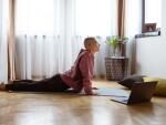 Woman performing a yoga pose on a mat with a laptop sitting on the floor nearby