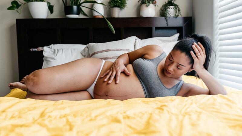 Pregnant female lying on bed holding lower part of belly