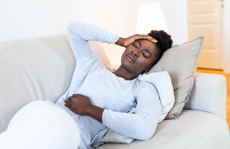 African American woman in pain on couch with hands on head and abdomen