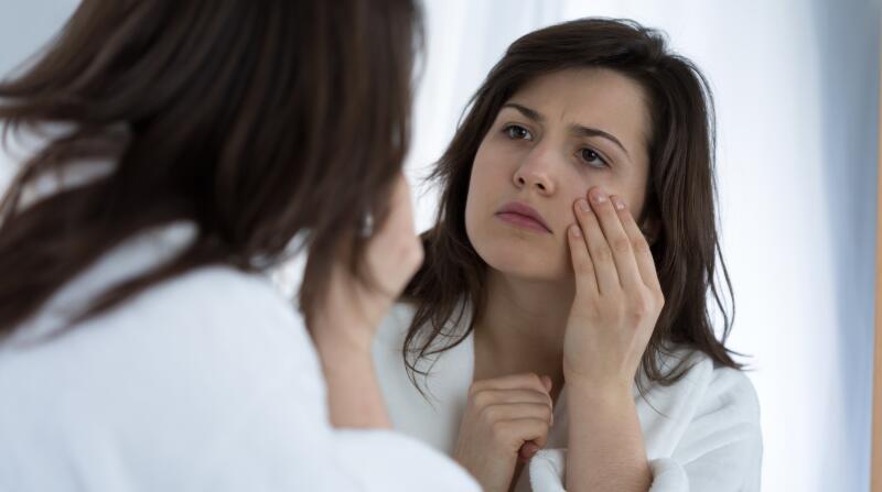 woman in bathroom looking at eyes in mirror
