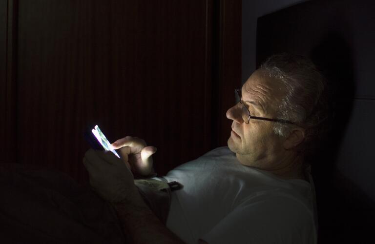 man awake bed with his smartphone