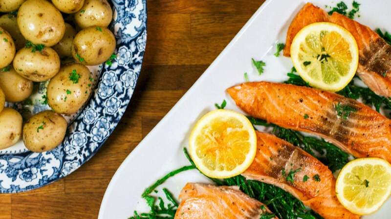 A plate of cooked salmon filets and lemons alongside a plate of potatoes.