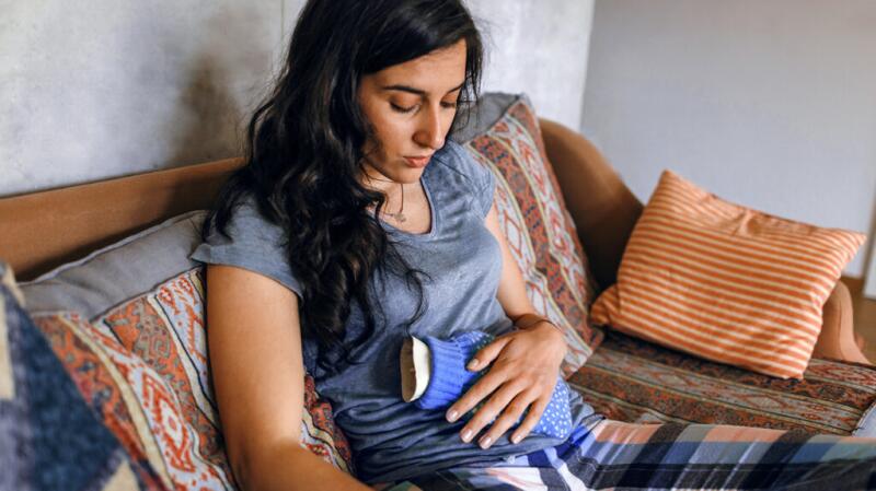 a woman is holding a hot water bottle to her stomach