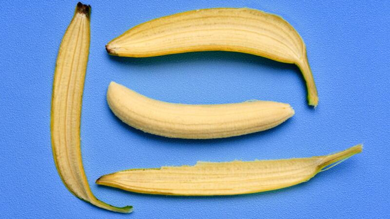 A peeled banana surrounded by the peel pieces against a blue background
