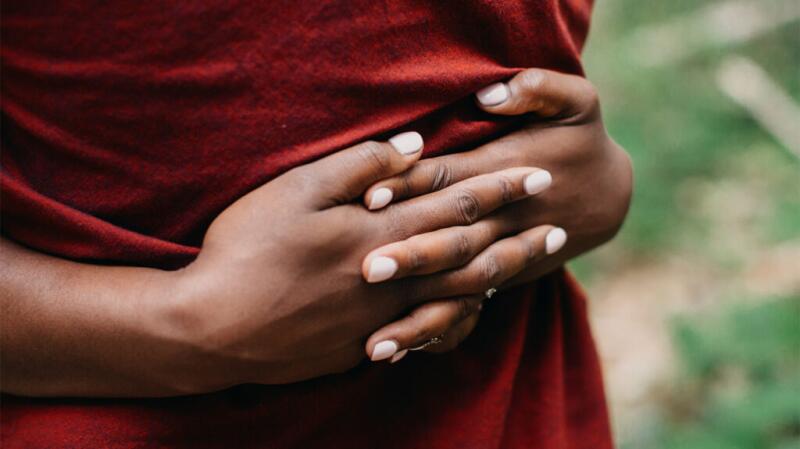 Unseen person standing outdoors with hands crossed over stomach