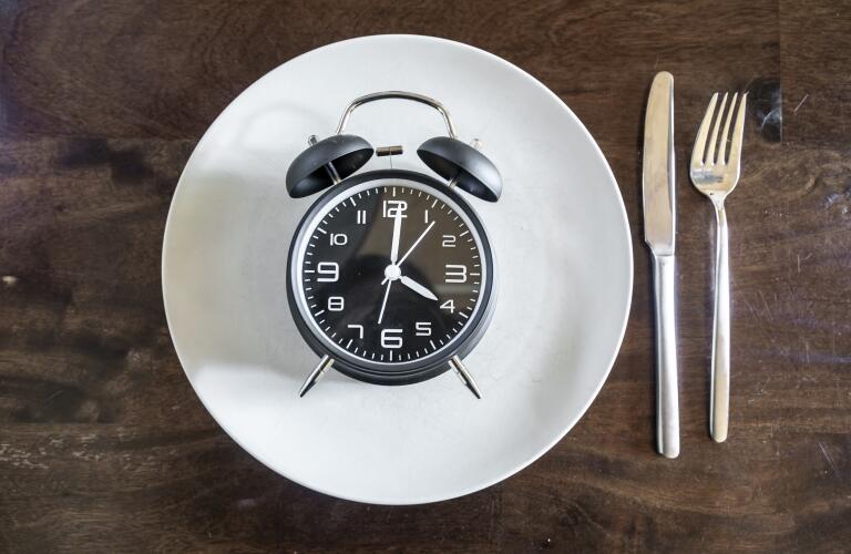 Image of alarm clock on empty dinner plate with knife and fork on table