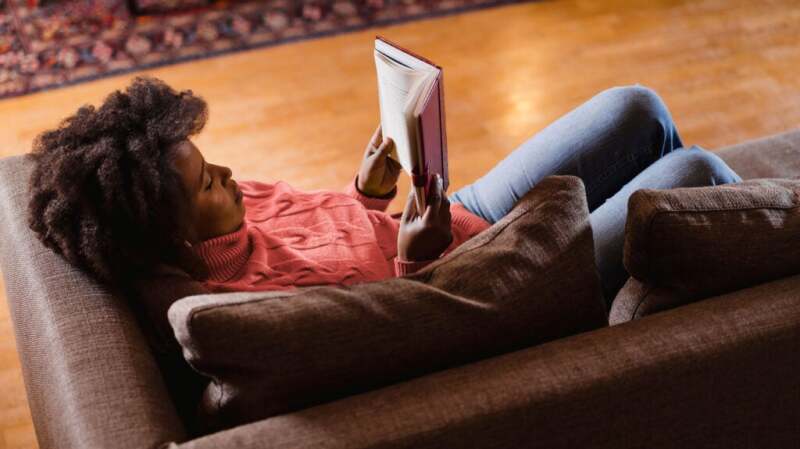 A woman laying on a couch and reading a book