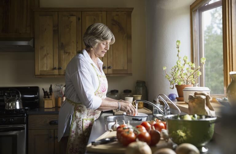 Senior woman washing vegetables at kitchen sink