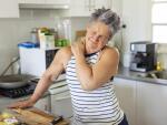 Fit senior Caucasian woman in home kitchen holding neck and shoulder in pain