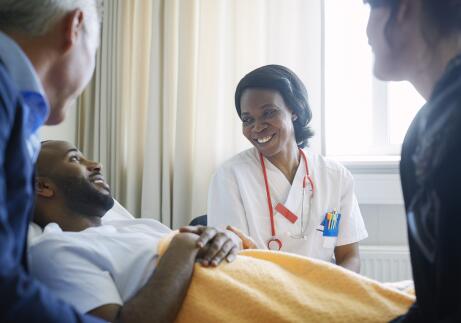 Smiling female doctor talking to patient and family in hospital ward