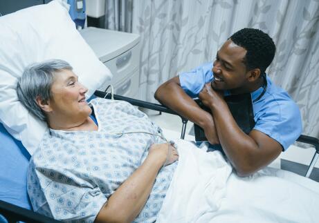 Young male African American doctor or nurse talking to older female Caucasian patient in hospital bed