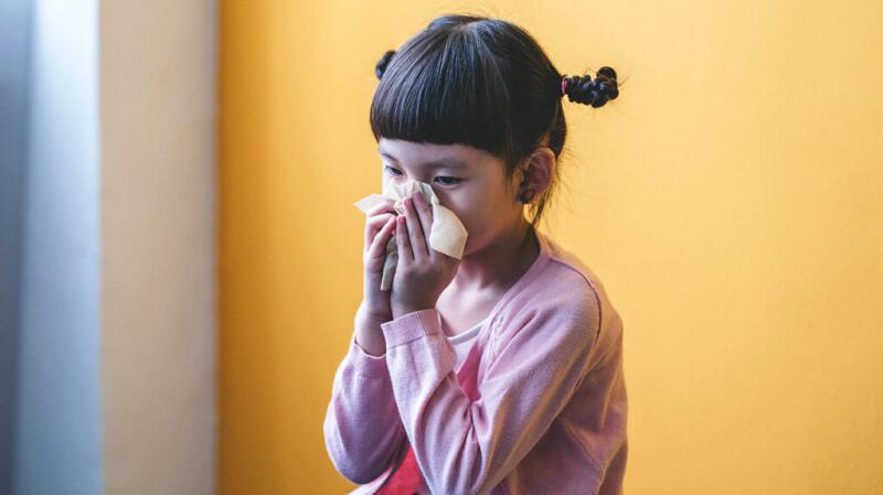 A young girl blows her nose into a tissue.