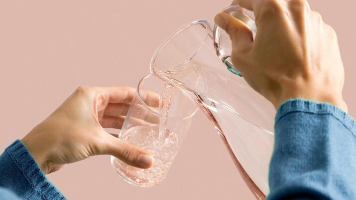 unidentifiable person's hands pouring water from a pitcher into a glass to drink