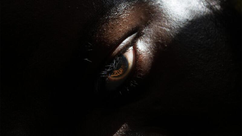 Extreme close-up of a person's face, showing a person's eye and upper face, highlighted by a beam of light.