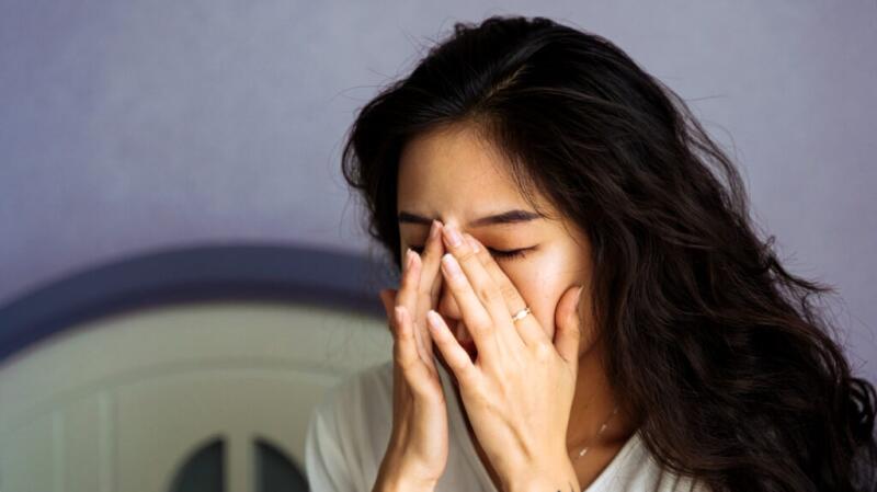 Woman rubs corners of eyes with her eyes closed