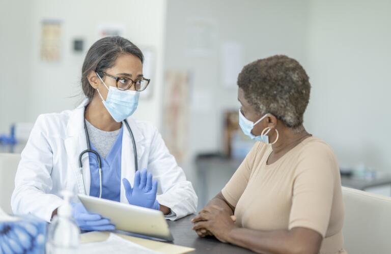 female doctor with digital tablet talking to female patient in medical exam