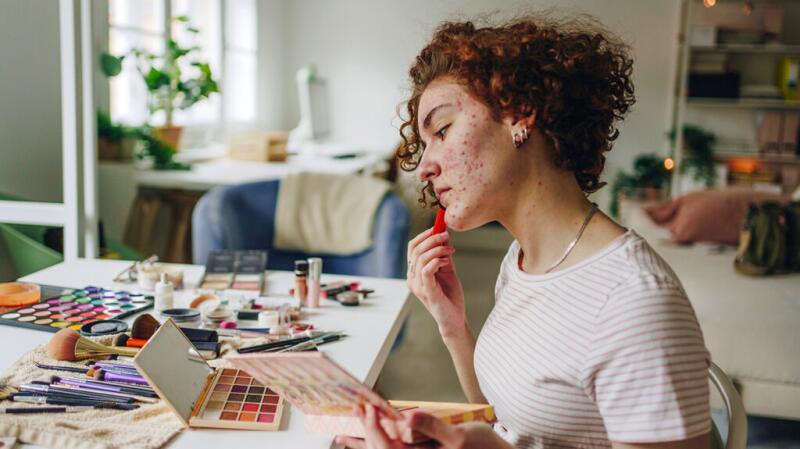A young woman with acne applying makeup