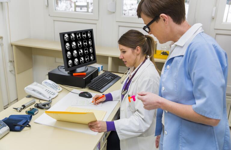 Two female Caucasian doctors reviewing files with CT scans on computer screen
