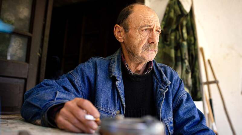 An older man sitting and holding a cigarette